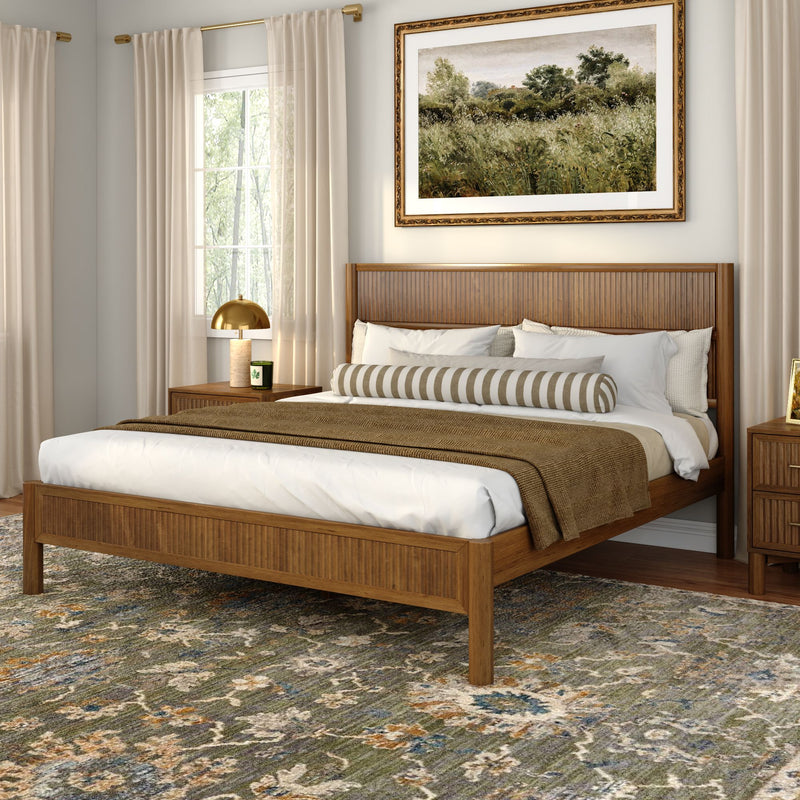 Modern bedroom with wooden slatted bed frame, neutral bedding and striped bolster, textured earth-tone area rug, framed landscape wall art, gold bedside lamp and sheer curtains