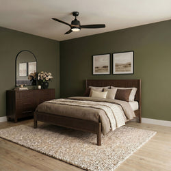 Modern bedroom with dark green accent wall, wooden bed and dresser, neutral beige bedding, woven rug and black ceiling fan with light