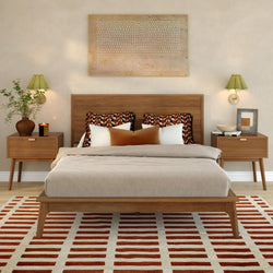 Mid-century modern bedroom with wood platform bed, neutral linens, patterned accent pillows, matching wood nightstands, wall sconces, and red-striped area rug