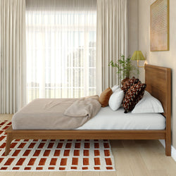Sunlit modern bedroom with wooden platform bed, neutral linen bedding, patterned throw pillows, sheer curtains, indoor plant and rust-and-white geometric area rug