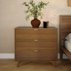 Mid-century modern three-drawer wooden dresser in a minimalist bedroom with a terracotta potted plant and lit scented candle on top
