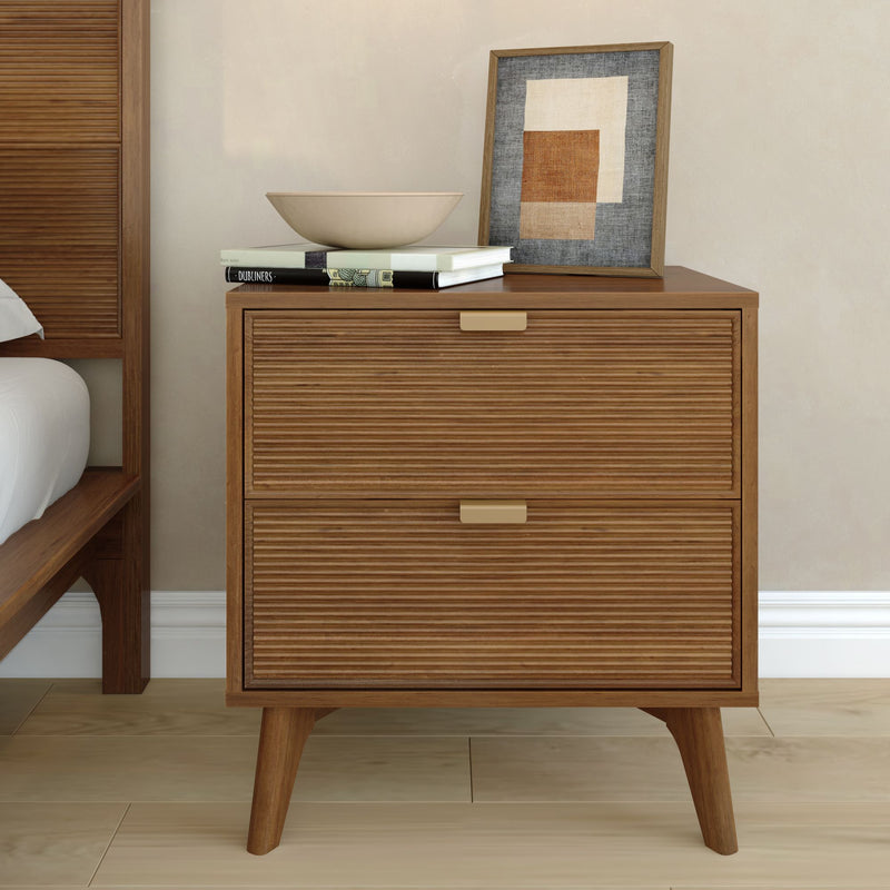 Mid-century modern wooden nightstand with two ribbed drawers, brass handles and a decorative bowl, books and framed abstract art on top in a minimalist bedroom