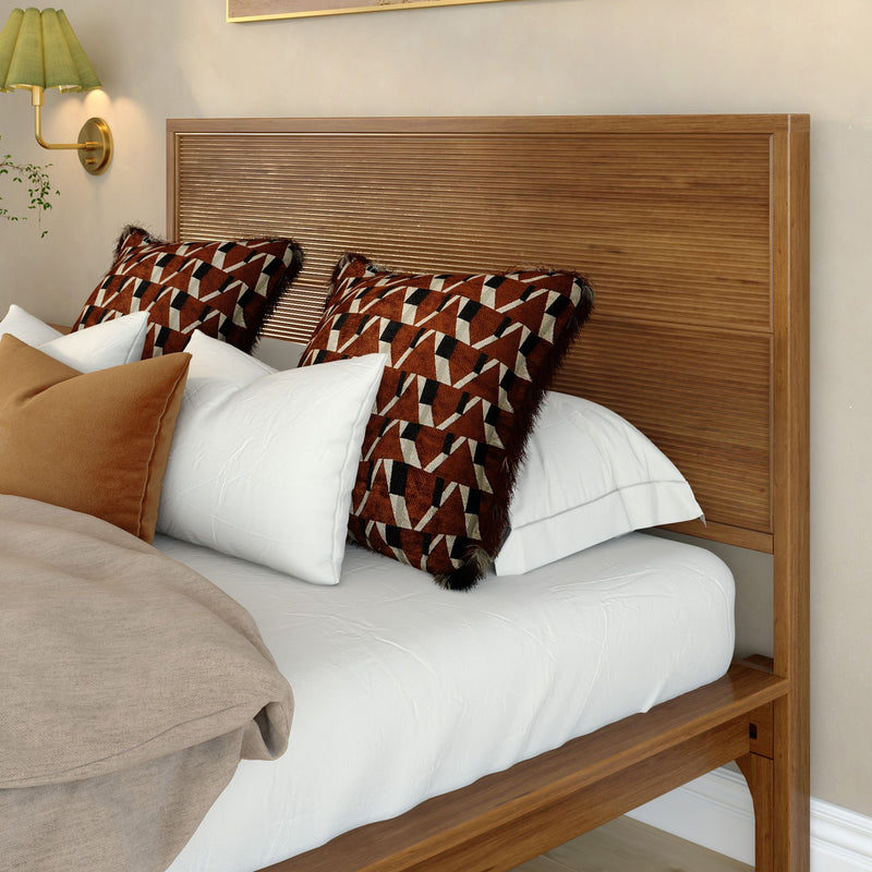 Cozy bedroom with modern wooden headboard, geometric rust-and-black throw pillows, crisp white bedding, beige linen throw and gold wall sconce