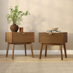 Minimalist Scandinavian interior with wooden nightstands, textured brown vase holding green foliage, patchouli scented candle and ceramic bowl on stacked books against a neutral beige wall