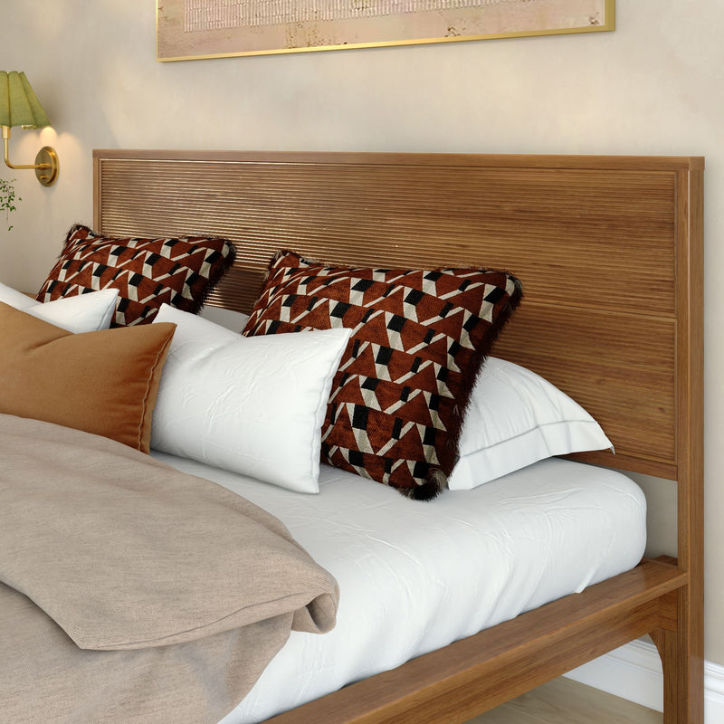 Modern wooden bed with slatted headboard, white sheets and beige linen duvet, rust-and-black geometric throw pillows and brass wall sconce in a cozy contemporary bedroom