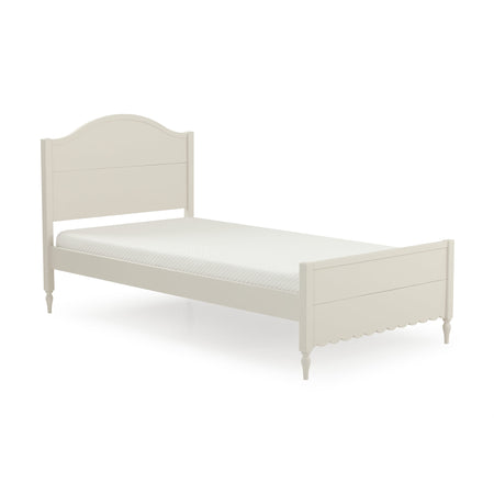 Cream-white wooden twin bed frame with arched headboard, scalloped footboard, turned legs and quilted mattress, farmhouse cottage style