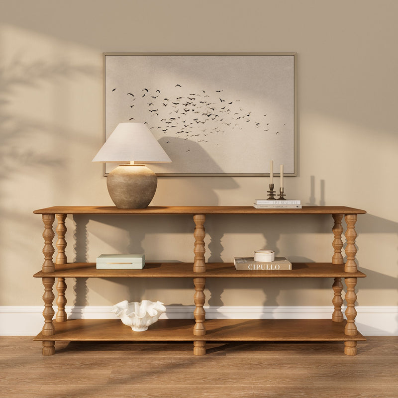Neutral entryway console table with turned wood legs, ceramic lamp with linen shade and framed bird wall art, styled with candles, books and shell bowl