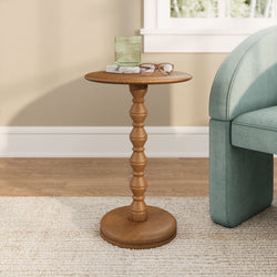 Wooden accent side table in living room with green ribbed glass on a marble coaster and reading glasses beside a teal upholstered sofa against a beige wall