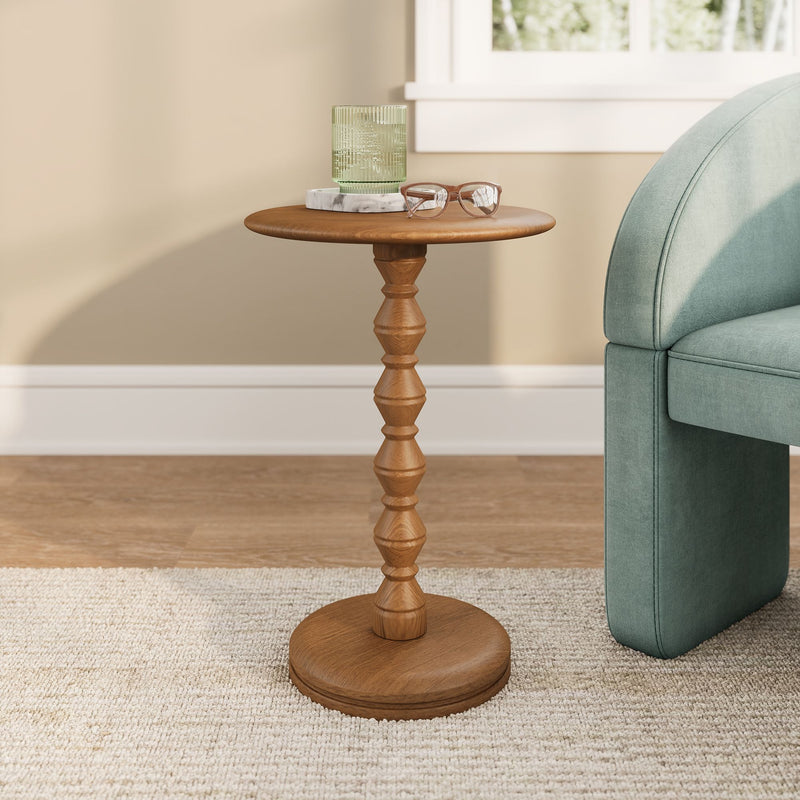 Wooden accent side table in living room with green ribbed glass on a marble coaster and reading glasses beside a teal upholstered sofa against a beige wall