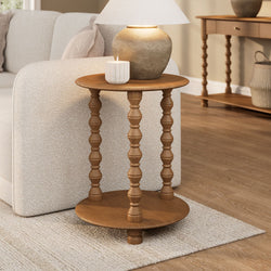 Close-up of a neutral living room showing a wooden spindle side table with a ceramic table lamp and lit white ribbed candle beside a beige sofa