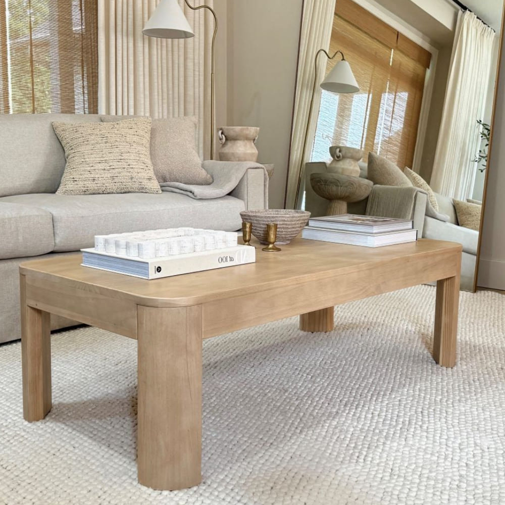 Wooden dining table set with green napkins and wine glasses on a rustic rug.