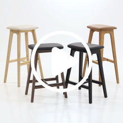 Modern wooden bar stools with cushioned seats in various finishes on a white background.