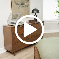 Mid-century modern walnut dresser in bright bedroom with vintage vinyl record player, matte black dome lamp, leather catchall, abstract wall art, green bedding and hardwood floor