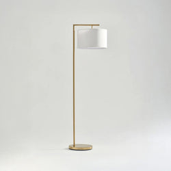 Modern gold floor lamp with white drum shade on minimalist background.
