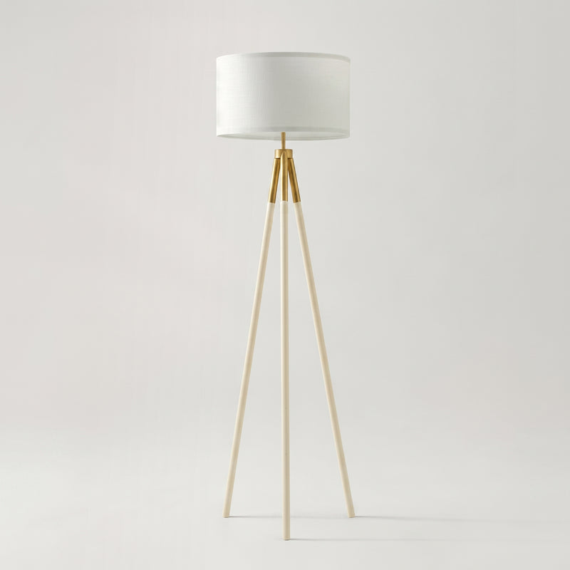 Modern tripod floor lamp with white drum shade and brass gold accents on neutral background, minimalist Scandinavian living room lighting