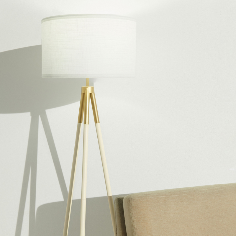 Modern tripod floor lamp with white drum shade and gold accents beside beige sofa in minimalist living room interior