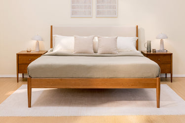 Minimalist mid-century modern wooden bed frame with neutral beige bedding, two matching nightstands and white table lamps in a serene bedroom