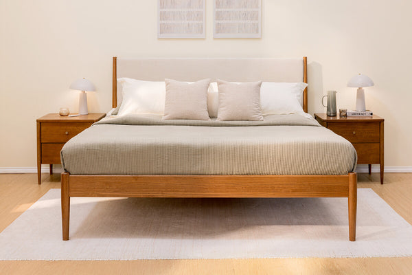 Minimalist mid-century modern wooden bed frame with neutral beige bedding, two matching nightstands and white table lamps in a serene bedroom