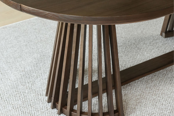 Round walnut dining table with vertical slatted pedestal base on textured beige rug — modern mid-century wooden dining table
