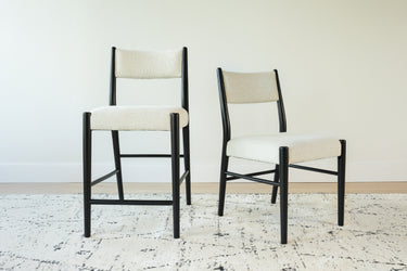 Set of two modern black-frame dining chairs with cream boucle upholstery on a patterned area rug in a minimalist room