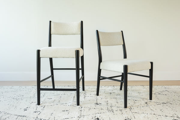 Set of two modern black-frame dining chairs with cream boucle upholstery on a patterned area rug in a minimalist room