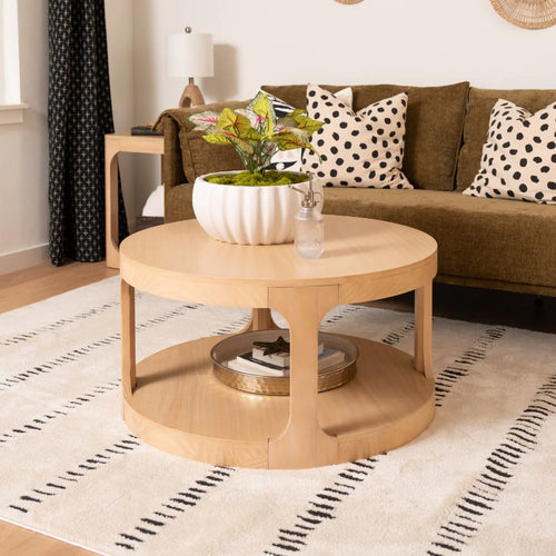 Round wooden coffee table with lower shelf and white planter, cozy modern living room with olive sofa, polka dot pillows, and neutral rug