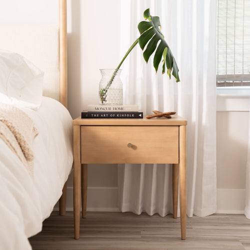 Wooden nightstand with books and a plant next to a bed in a bedroom.