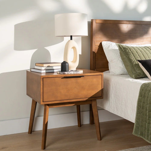 Wooden nightstand with lamp next to a bed with green and white bedding.