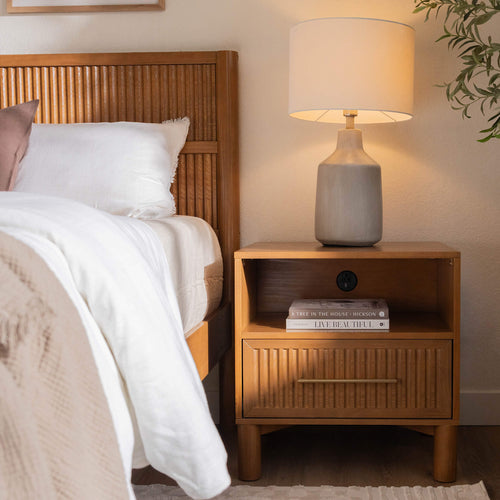 Cozy modern bedroom interior with ceramic bedside lamp on wooden nightstand, slatted wood headboard and white linen bedding