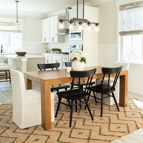 Modern kitchen with wooden dining table and black chairs, white cabinets, and a patterned rug.