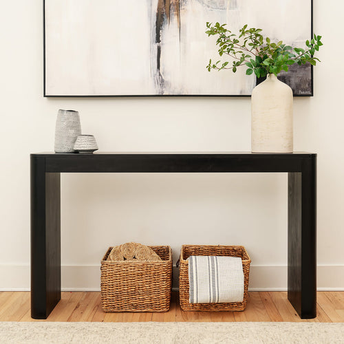 Modern black console table in entryway with large ceramic vase of greenery, two decorative stoneware vases on top and two wicker storage baskets with a striped throw underneath