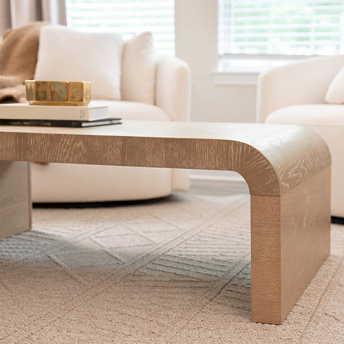 Minimalist neutral living room with curved oak coffee table, beige sofa, textured rug and brass candle