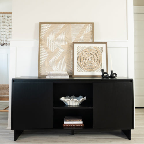 Modern black console table with open shelving featuring a white decorative bowl, stacked coffee table books, black sculptural candleholders and neutral woven framed wall art leaning against a white shiplap wall — minimalist living room decor and entryway storage