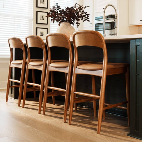 Modern kitchen island with four wooden bar stools with leather cushions, white quartz countertop, ceramic vase with foliage and stainless steel pull-down faucet