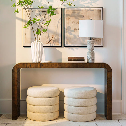 Minimalist entryway: wooden console table with white ceramic vase and leafy branches, framed abstract art, stone lamp and cream boucle ottomans — modern neutral home decor