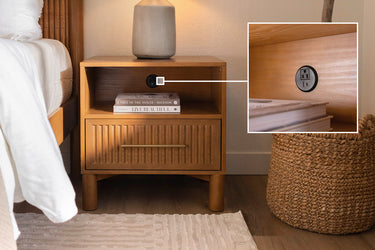Wooden nightstand with built-in power outlet, ceramic lamp, stacked books and woven basket in cozy modern bedroom