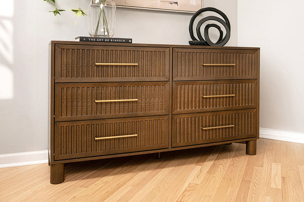 Mid-century modern six-drawer brown wooden dresser with ribbed drawer fronts and brass handles on light hardwood floor in a styled bedroom