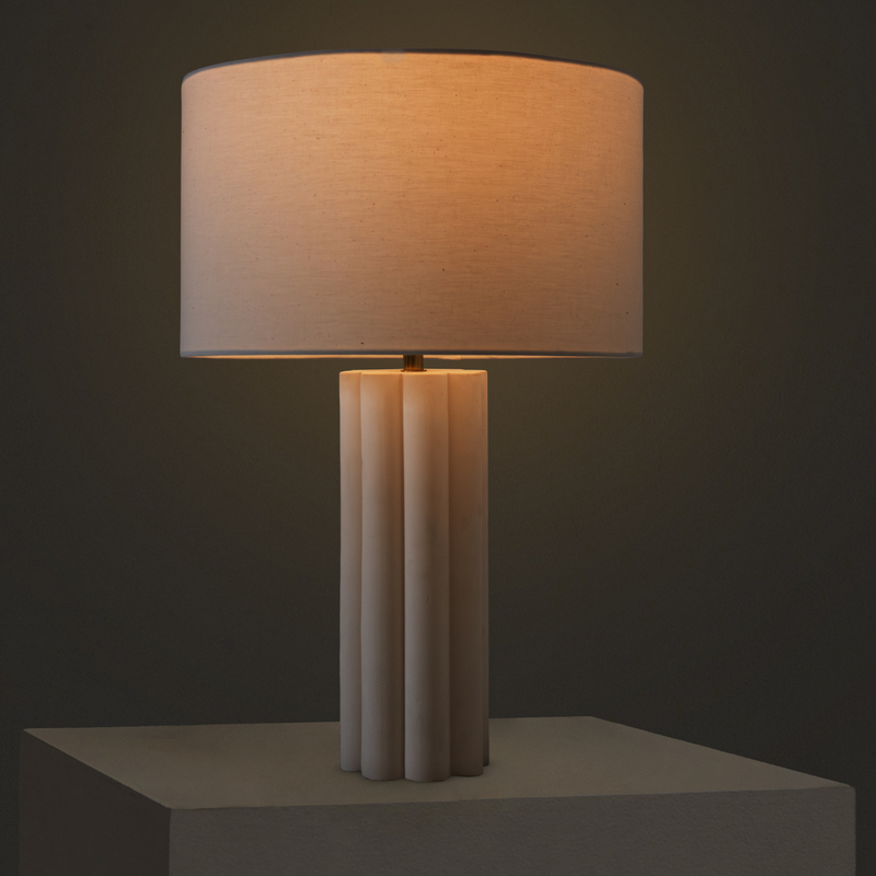 Modern table lamp with beige linen drum shade and fluted marble column base on pedestal, warm ambient lighting for minimalist bedroom or living room decor