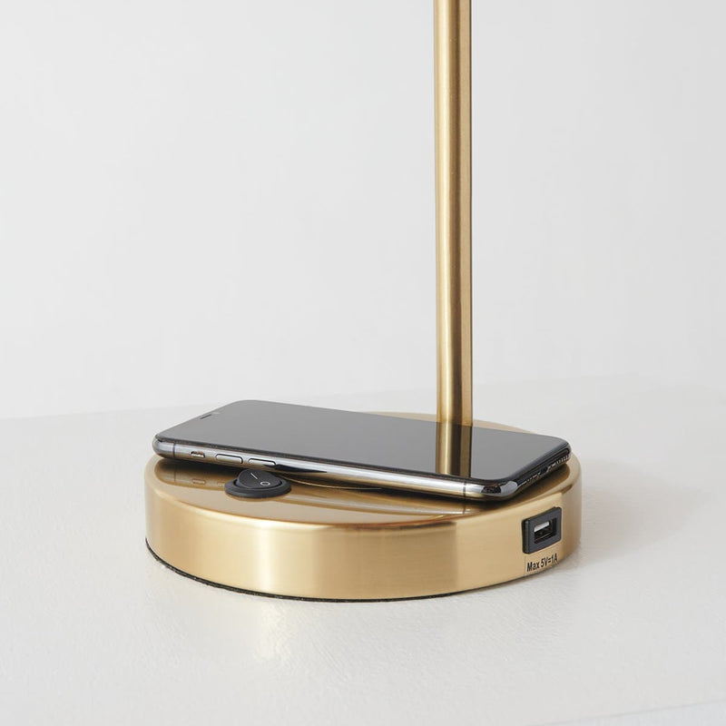 Modern gold desk lamp with wireless charging base and USB port, smartphone placed on base charging