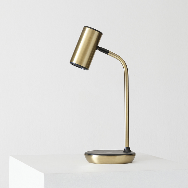 Brass adjustable desk lamp with curved arm and cylindrical shade on white pedestal, modern minimalist bedside or office reading lamp