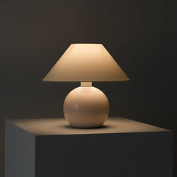 Minimalist ceramic table lamp with beige fabric shade on pedestal, warm ambient lighting for modern bedside or living room decor