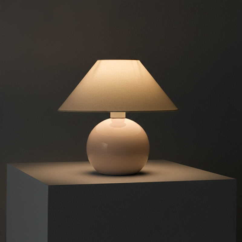 Minimalist ceramic table lamp with beige fabric shade on pedestal, warm ambient lighting for modern bedside or living room decor