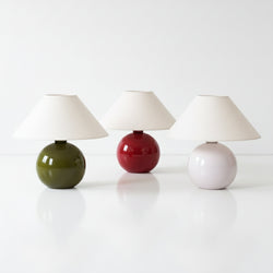 Modern ceramic table lamps — three round bases in olive green, red, and pale pink with white cone shades on a glossy white surface