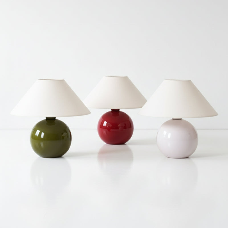 Modern ceramic table lamps — three round bases in olive green, red, and pale pink with white cone shades on a glossy white surface