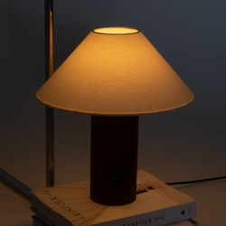 Modern wooden-base bedside table lamp with beige fabric shade casting warm ambient light on stacked Kinfolk books