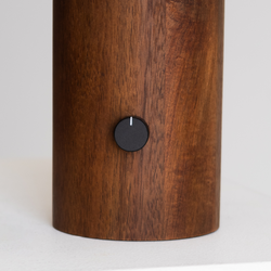 Walnut wood cylindrical base with matte black rotary knob on white surface, minimalist modern home decor