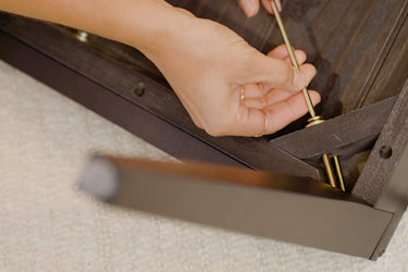 Person assembling furniture with a screwdriver on a carpeted floor.