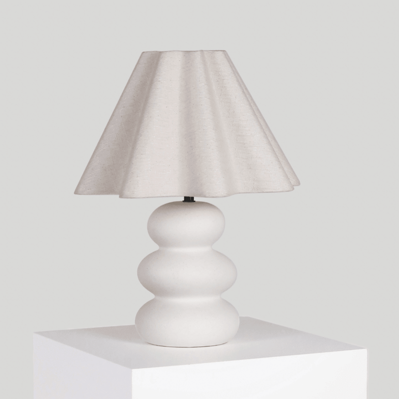 Elegant white table lamp with a sculptural base and fabric lampshade on a white pedestal.