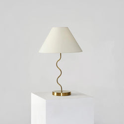 Elegant gold table lamp with a wavy design and white lampshade on a pedestal.