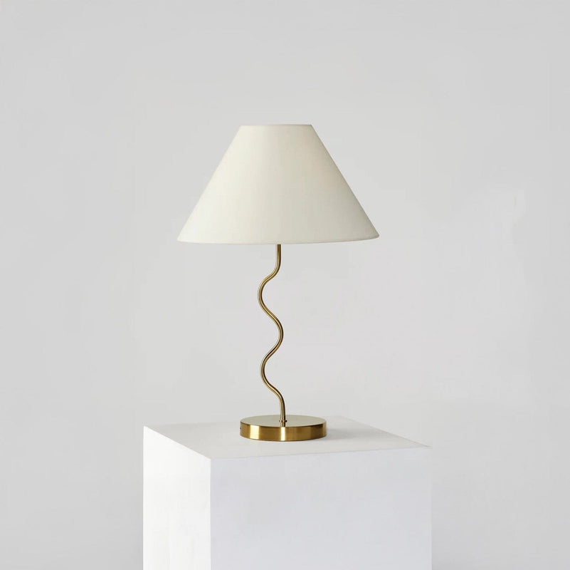 Elegant gold table lamp with a wavy design and white lampshade on a pedestal.